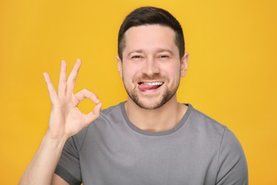 Happy man showing his tongue and OK gesture on orange background