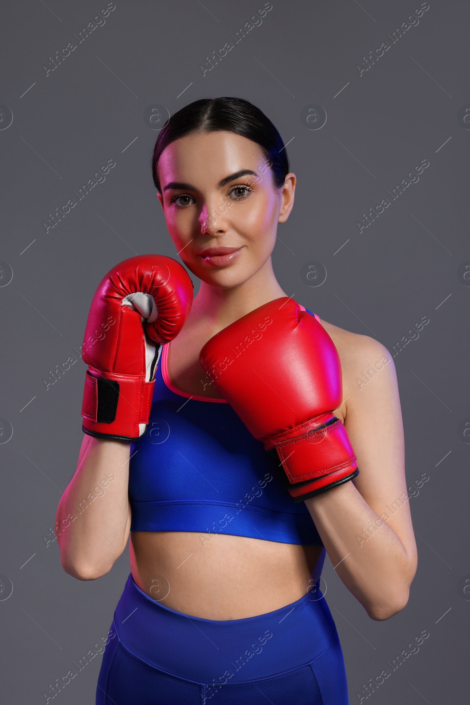 Photo of Portrait of beautiful woman wearing boxing gloves in color lights on grey background