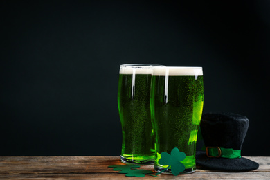 Photo of Green beer, hat and clover leaves on wooden table against black background, space for text. St. Patrick's Day celebration