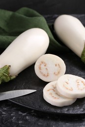 Photo of Board, raw white eggplants and knife on black table, closeup