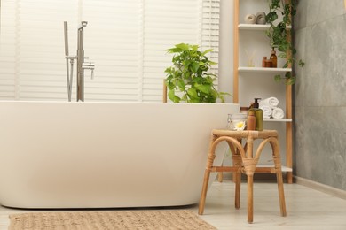 Stylish bathroom interior with ceramic tub, spa products and green houseplants