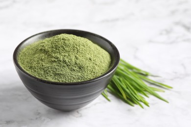 Photo of Wheat grass powder in bowl and fresh sprouts on white marble table, closeup