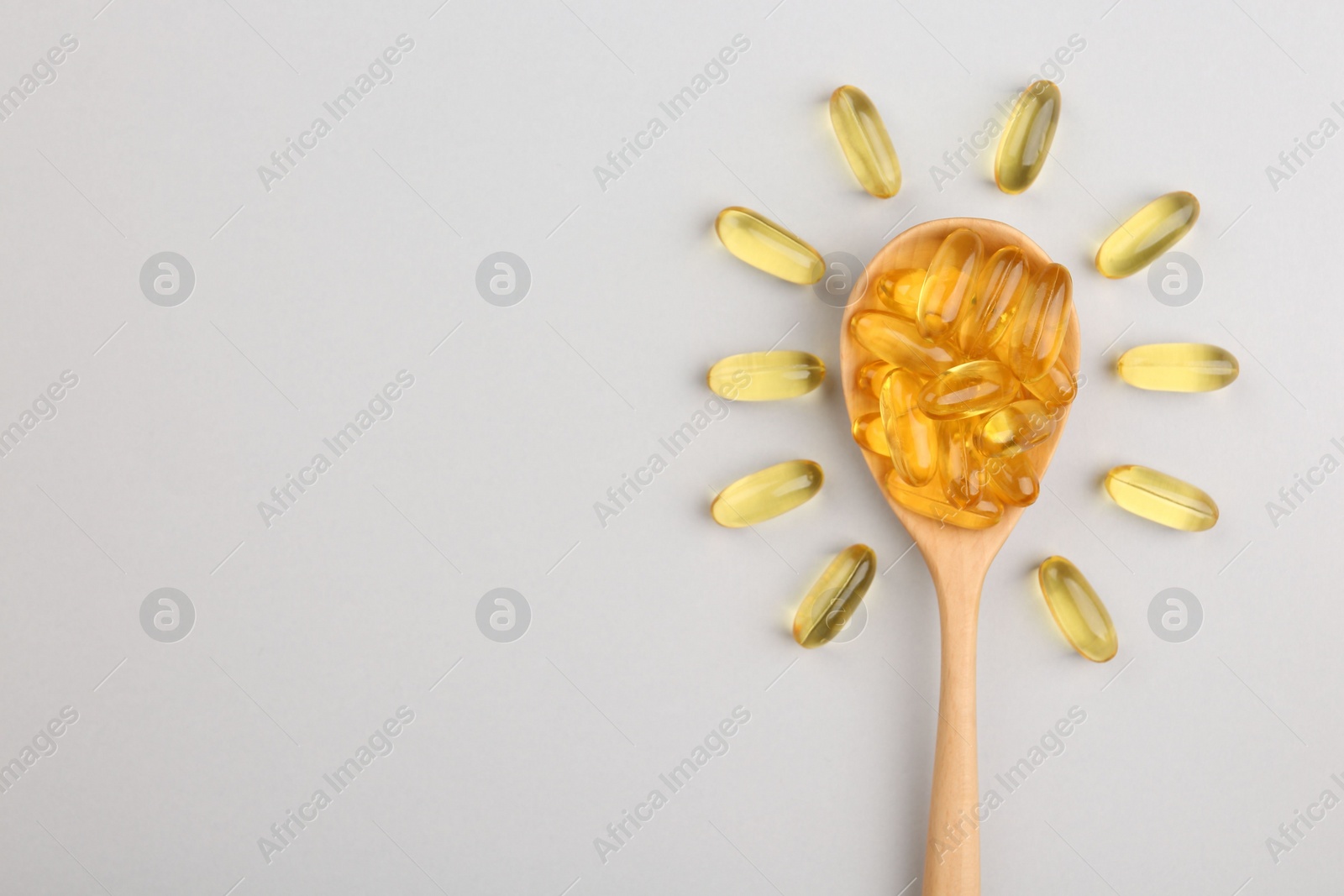 Photo of Wooden spoon with vitamin capsules on light background, top view. Space for text