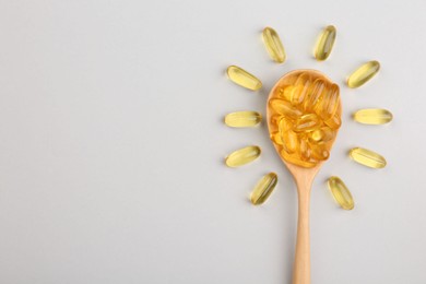 Wooden spoon with vitamin capsules on light background, top view. Space for text