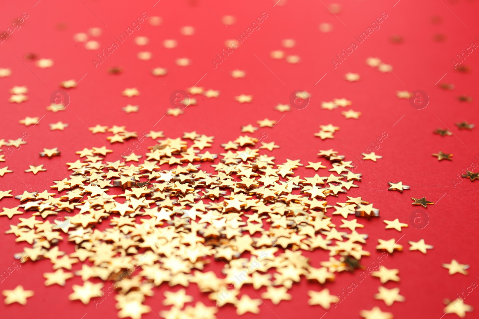 Photo of Gold confetti stars on red background, closeup. Christmas celebration