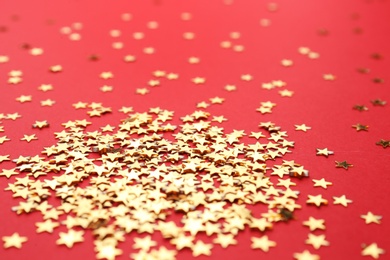 Photo of Gold confetti stars on red background, closeup. Christmas celebration