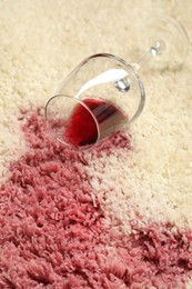 Photo of Overturned glass and spilled red wine on beige carpet, closeup