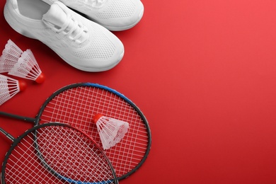 Photo of Badminton rackets, shuttlecocks and shoes on red background, flat lay. Space for text