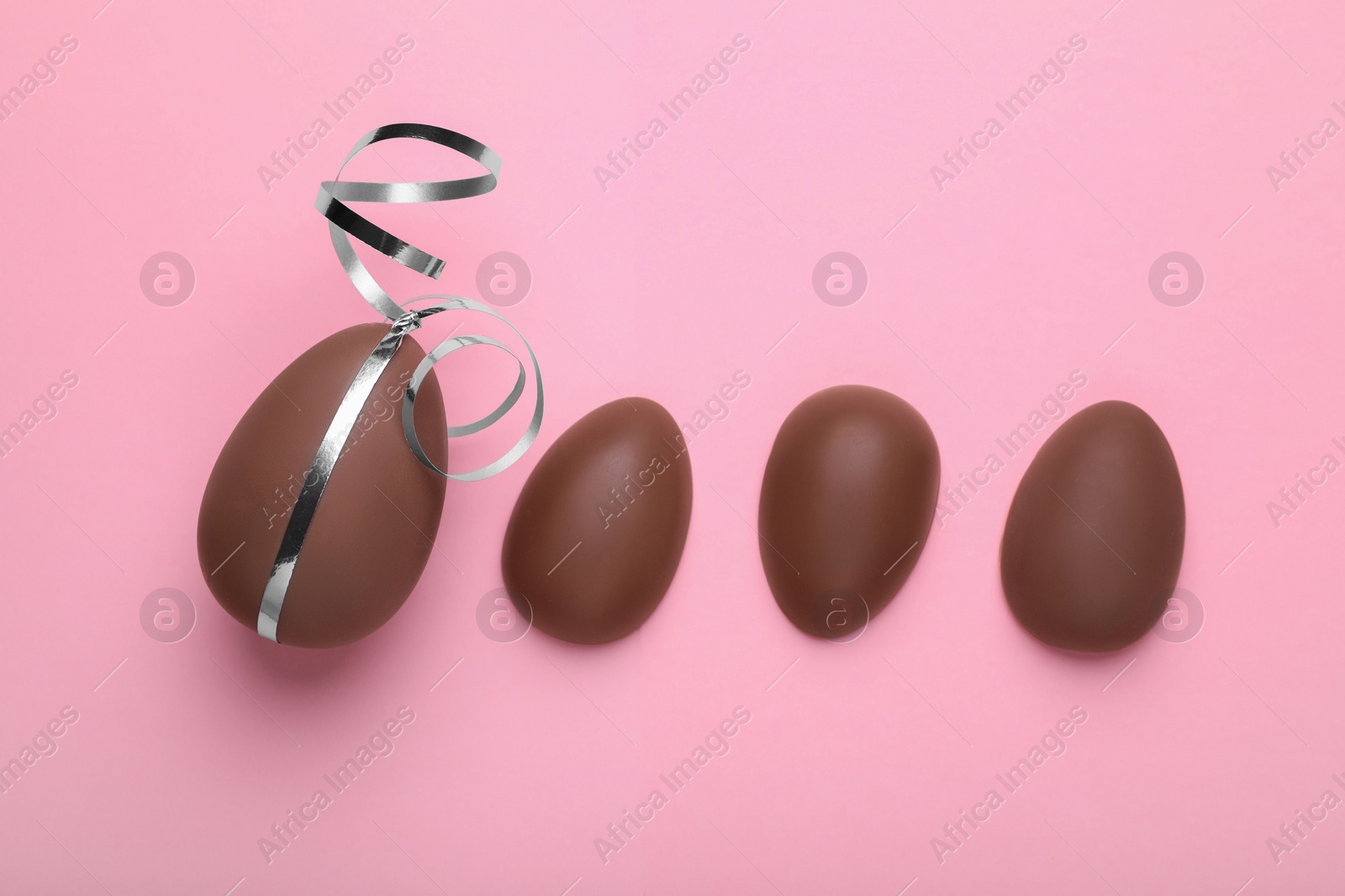 Photo of Whole and halves of chocolate eggs on pink background, flat lay