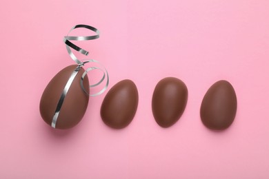 Photo of Whole and halves of chocolate eggs on pink background, flat lay