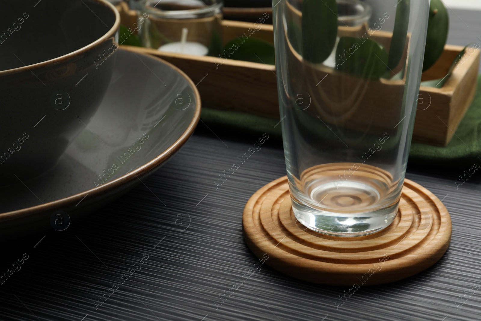Photo of Place setting with glass and drink coaster on black wooden table, closeup view