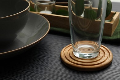 Place setting with glass and drink coaster on black wooden table, closeup view