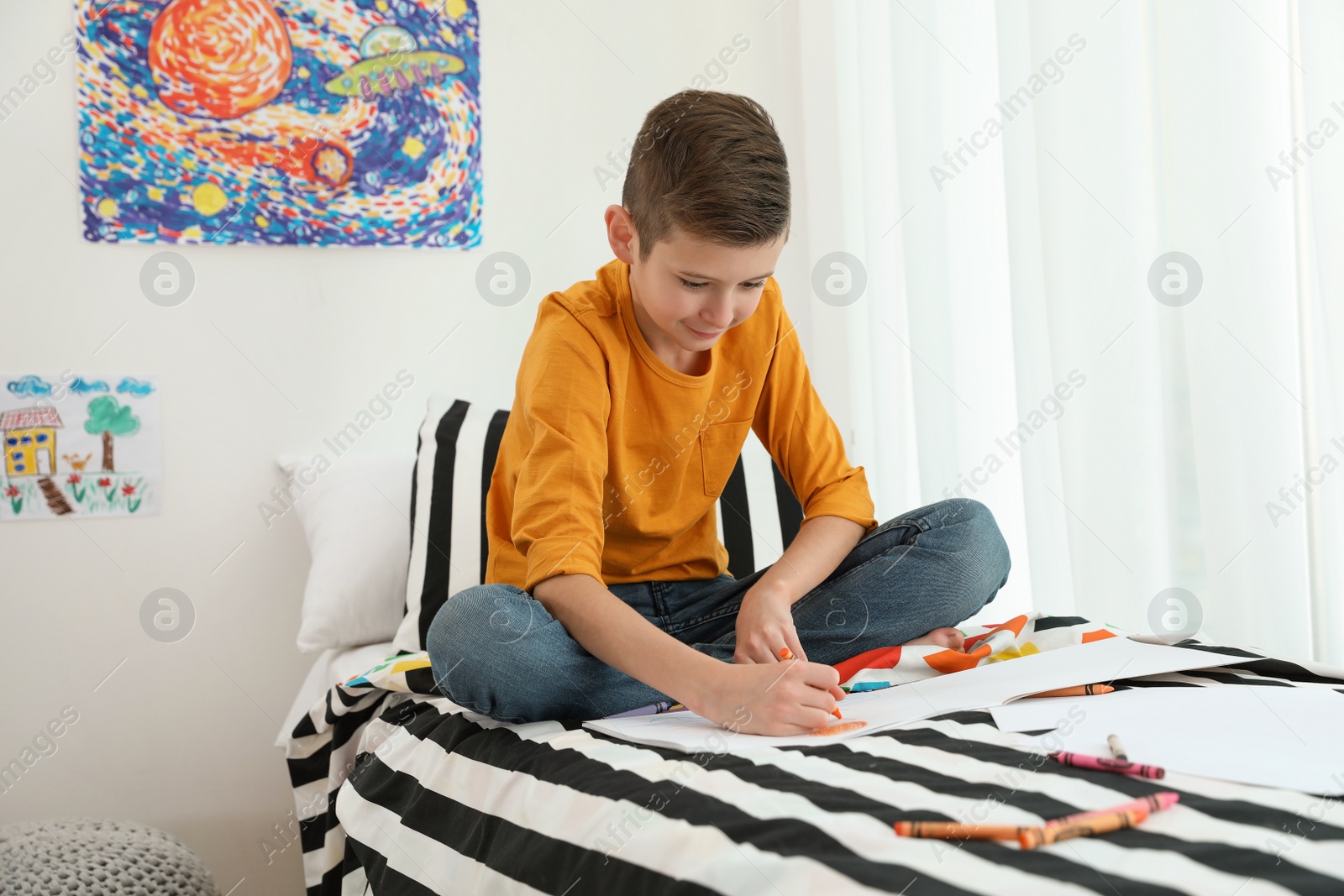Photo of Little boy drawing picture on bed indoors