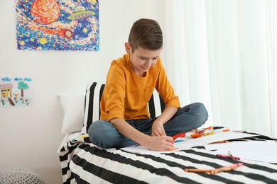 Photo of Little boy drawing picture on bed indoors