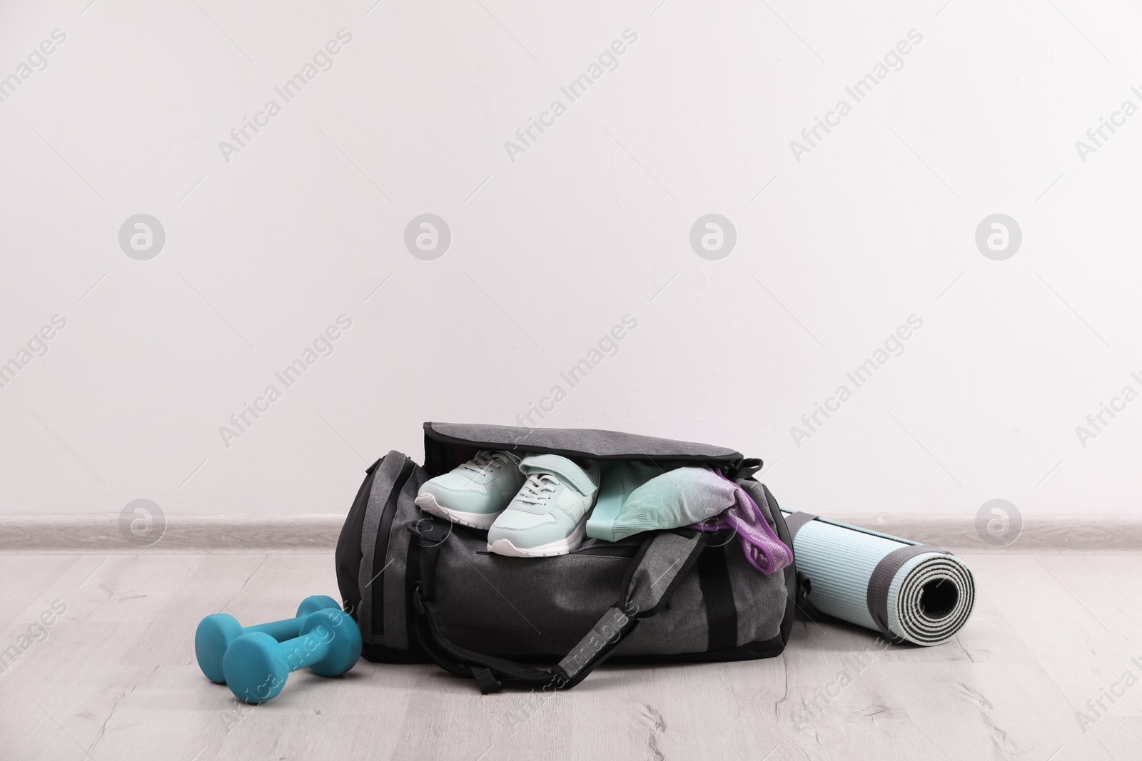 Photo of Grey bag and sports accessories on floor near white wall, space for text