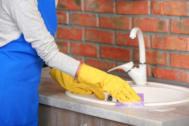 Photo of Woman cleaning kitchen sink with sponge, closeup