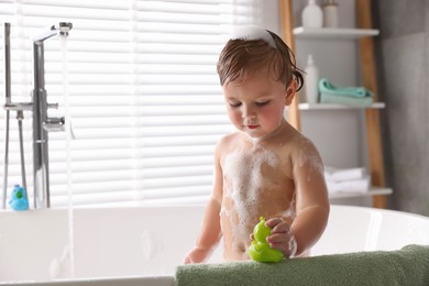 Photo of Cute little girl taking bubble bath with toy indoors. Space for text