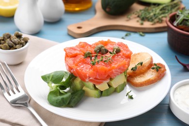 Photo of Delicious salmon tartare served with avocado and croutons on light blue table