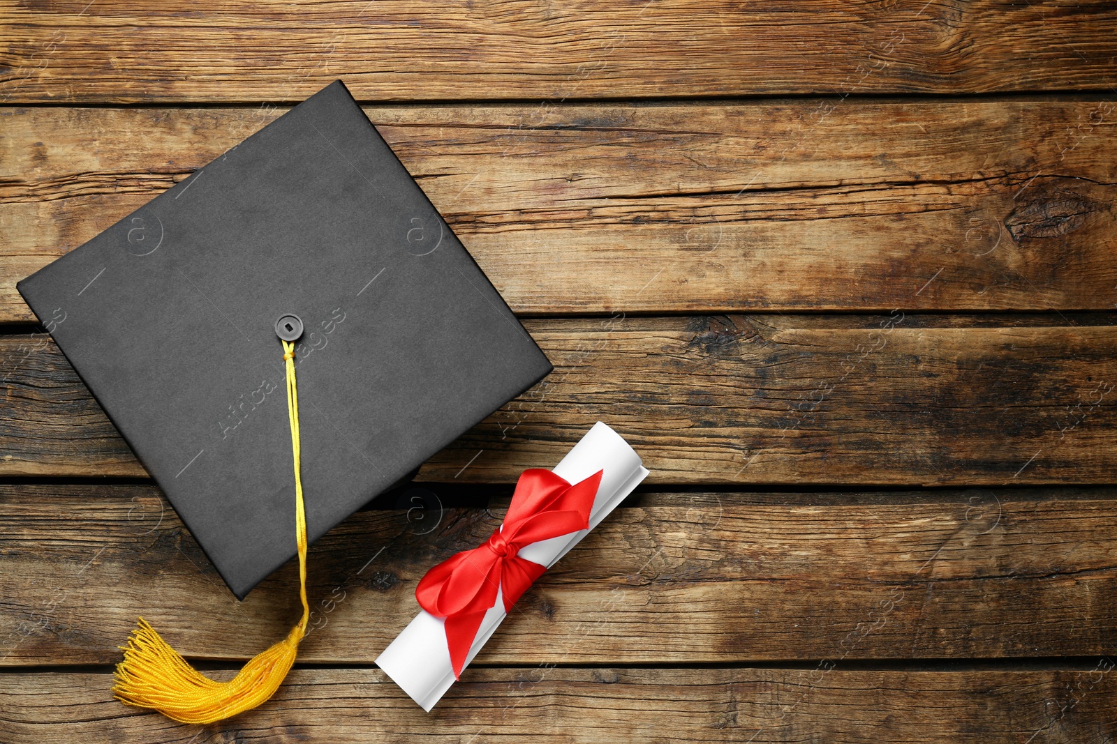 Photo of Graduation hat and diploma on wooden table, flat lay. Space for text