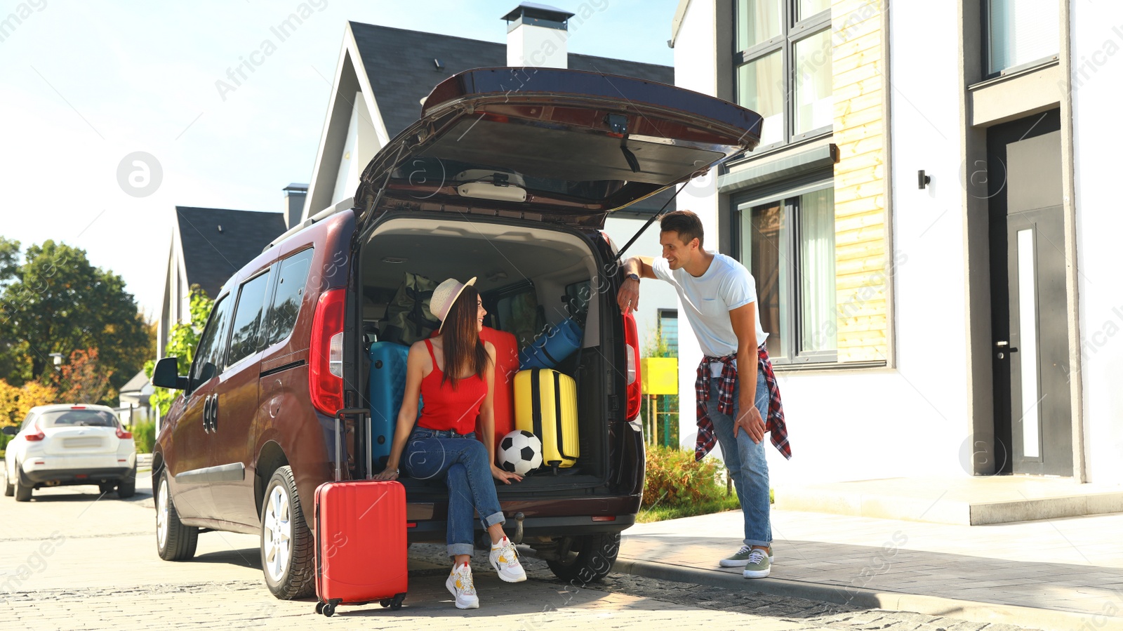 Photo of Young couple near car with suitcases in trunk outdoors. Moving day