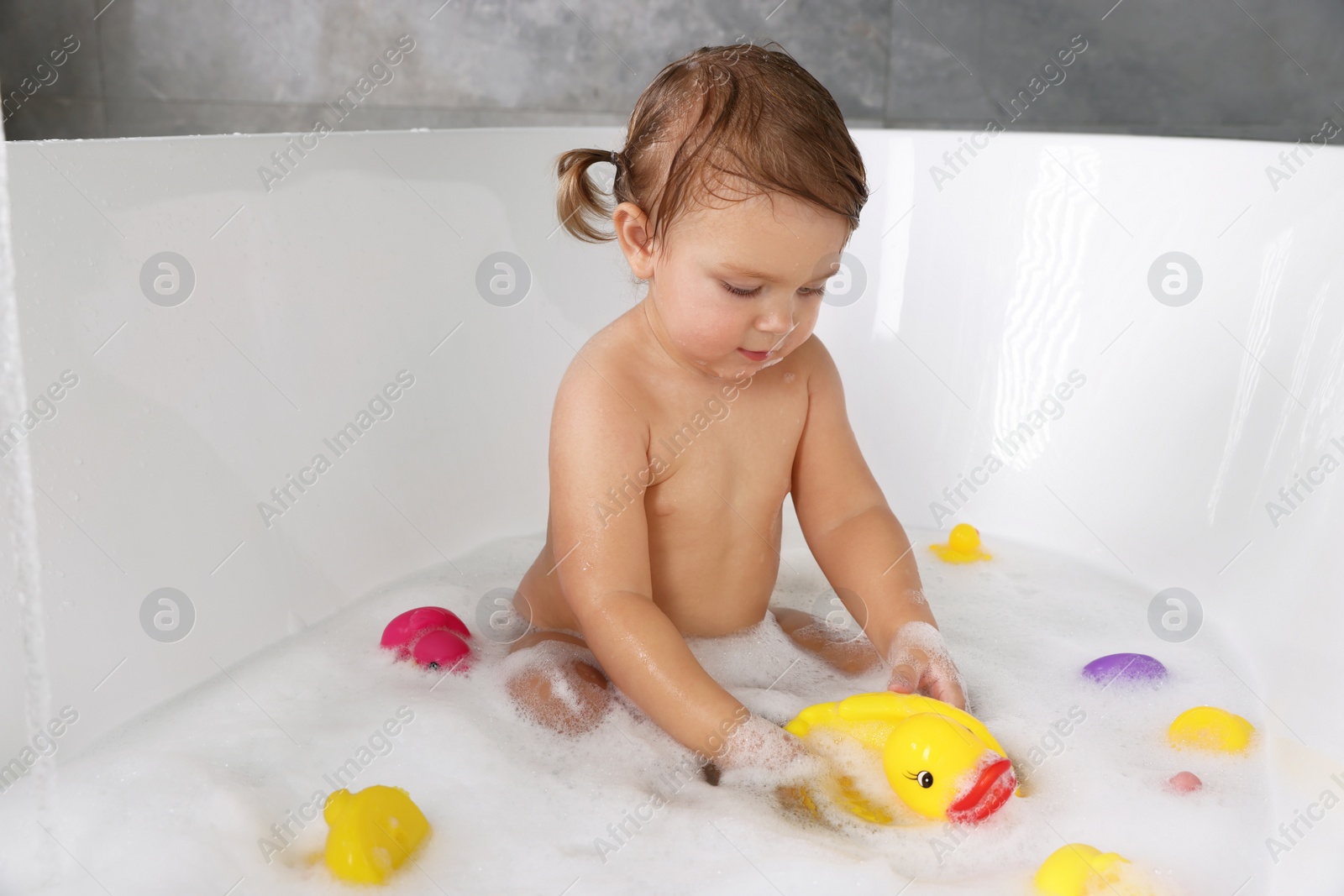 Photo of Cute little girl taking bubble bath with toys indoors