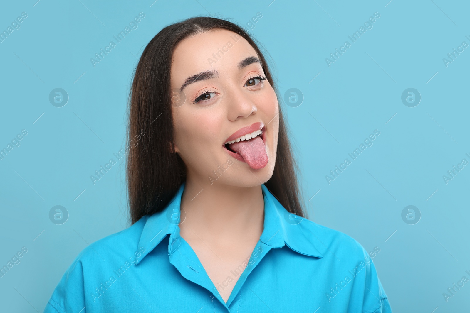 Photo of Happy woman showing her tongue on light blue background