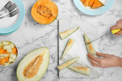 Photo of Woman cutting fresh tasty melon on board at table, top view