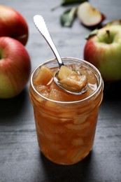 Tasty apple jam with spoon in glass jar and fresh fruits on grey table