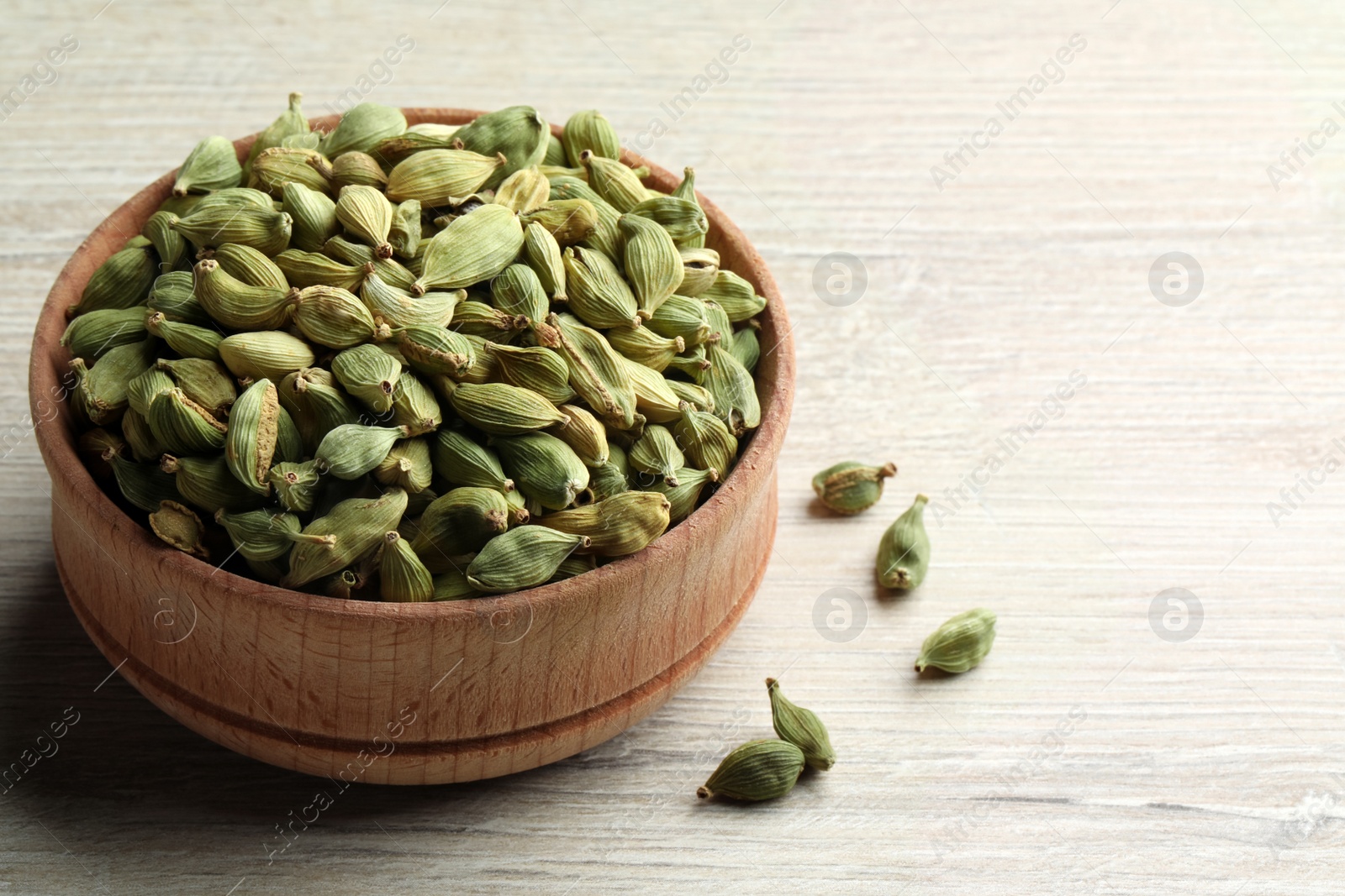Photo of Bowl of dry cardamom pods on white wooden table, closeup. Space for text