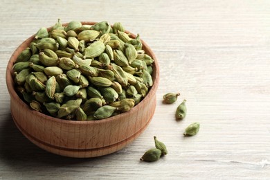 Bowl of dry cardamom pods on white wooden table, closeup. Space for text