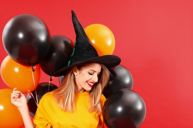 Photo of Beautiful woman wearing witch costume with balloons for Halloween party on red background