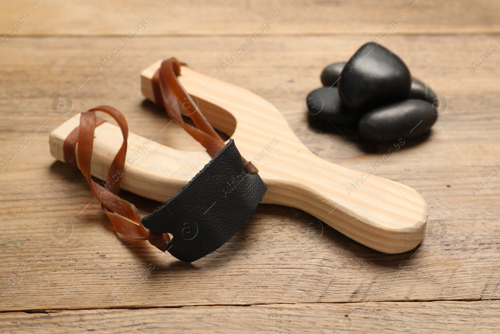 Photo of Slingshot with stones on wooden table, closeup