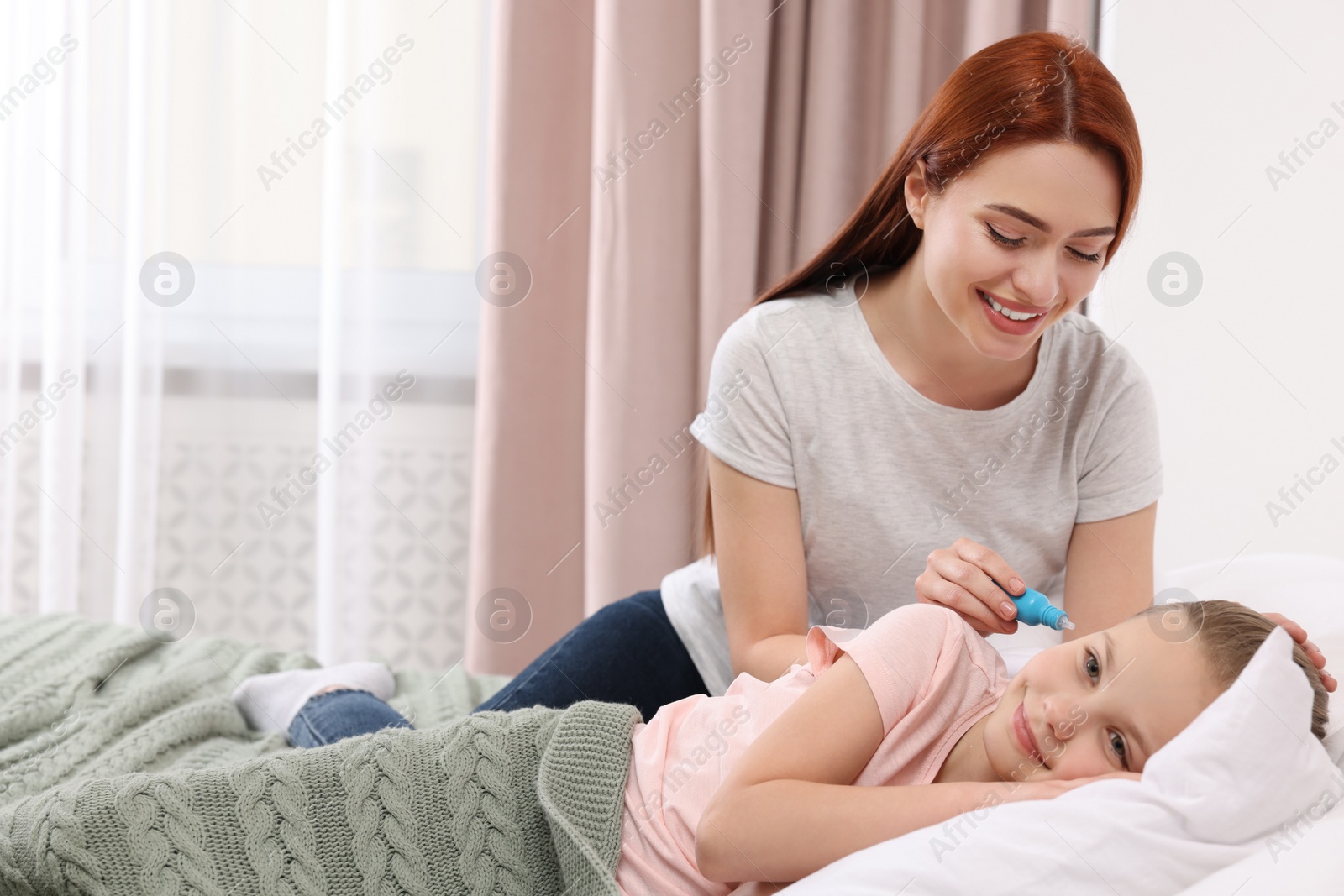 Photo of Mother dripping medication into daughter's ear in bedroom