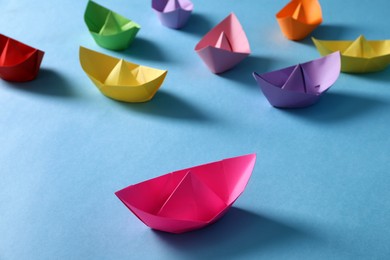 Photo of Bright pink paper boat standing out from colorful ones on light blue background. Diversity concept