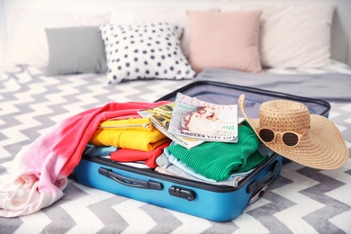 Photo of Open suitcase with different personal stuff on bed