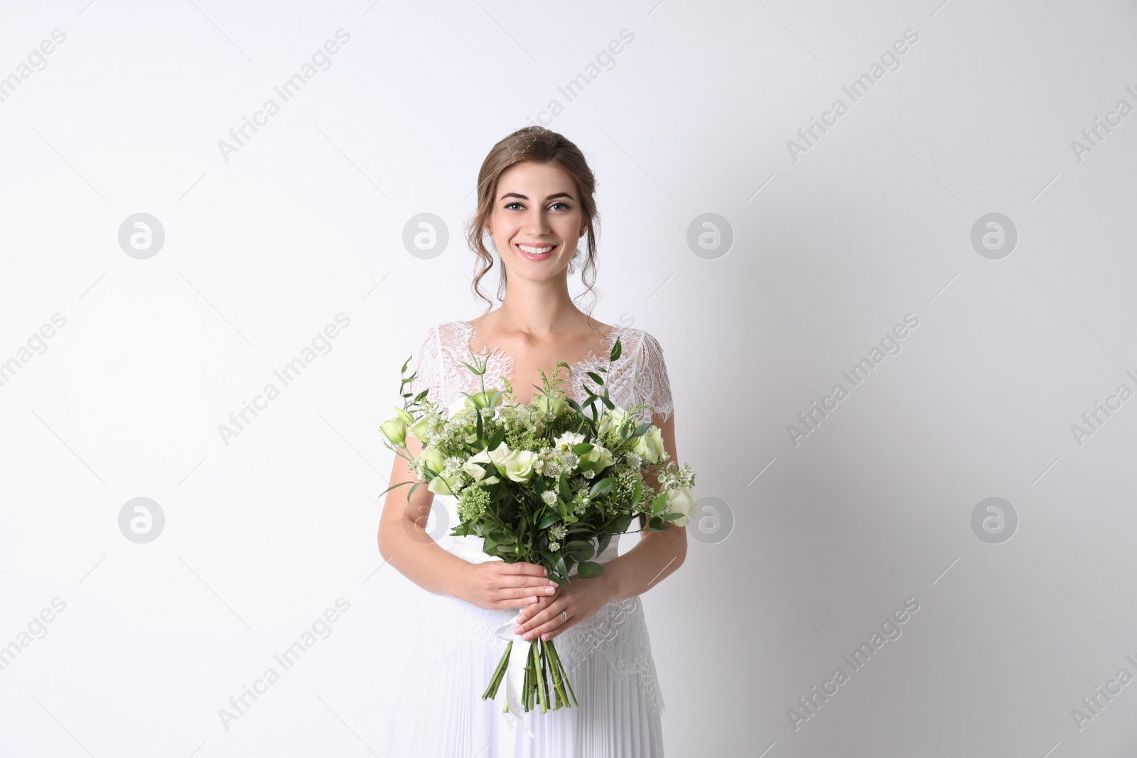 Photo of Young bride wearing wedding dress with beautiful bouquet on light background