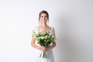 Young bride wearing wedding dress with beautiful bouquet on light background