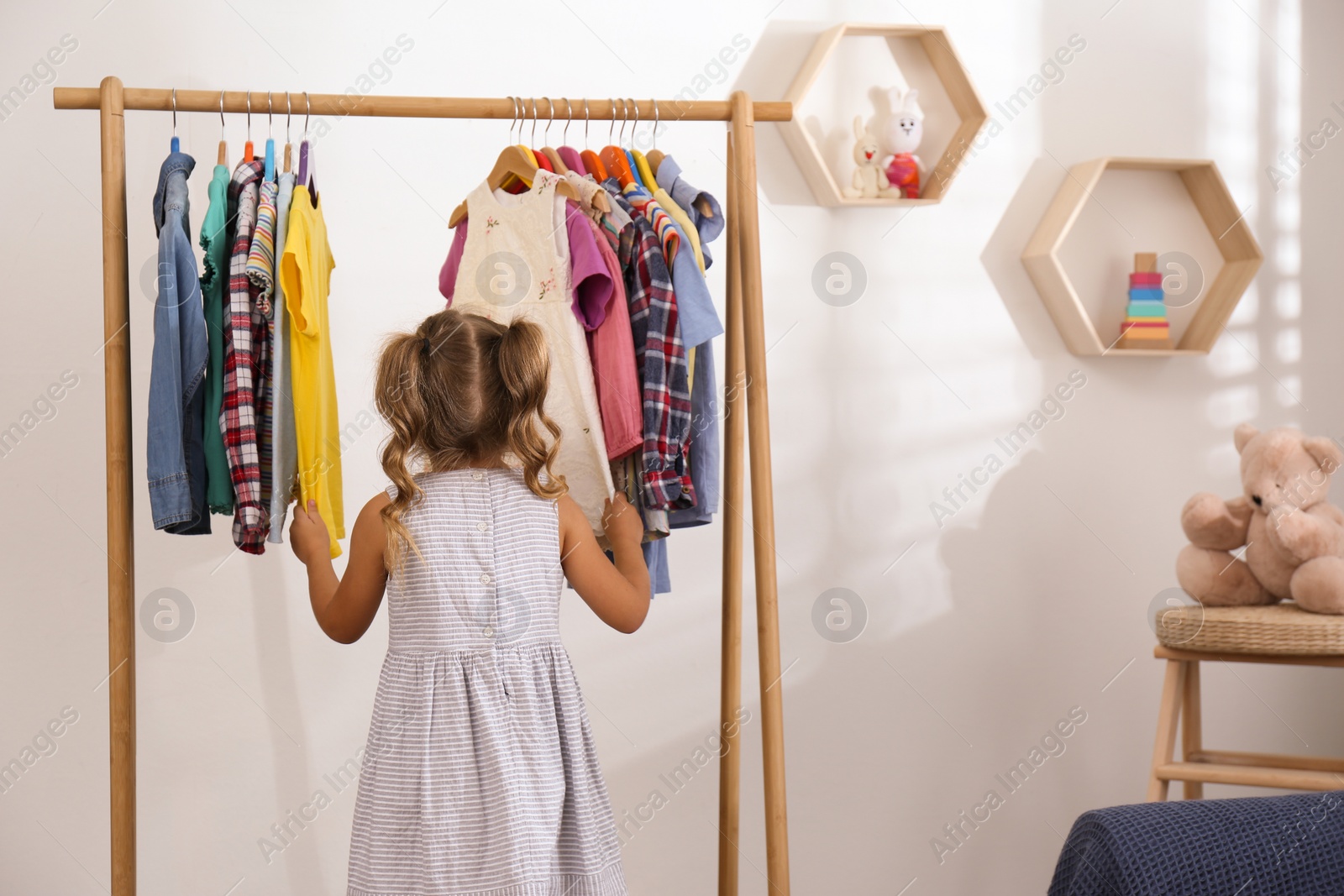 Photo of Little girl choosing clothes on rack in room