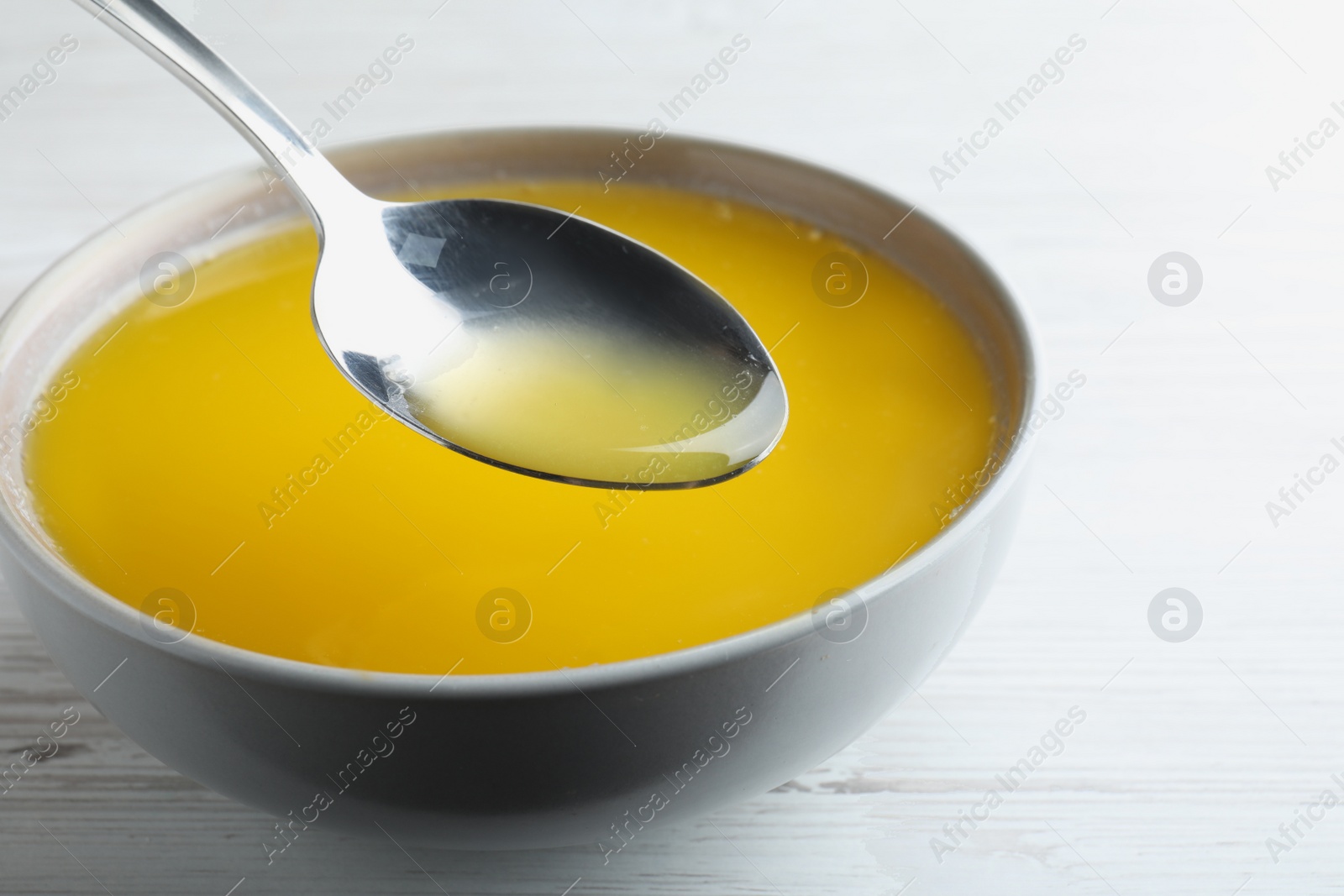 Photo of Spoon of clarified butter over bowl on white wooden table, closeup