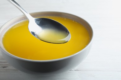 Spoon of clarified butter over bowl on white wooden table, closeup