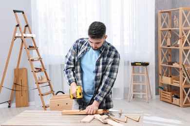 Young handyman working with electric drill at table in workshop