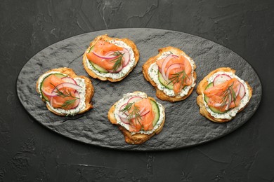 Tasty canapes with salmon, cucumber, radish and cream cheese on black table, top view