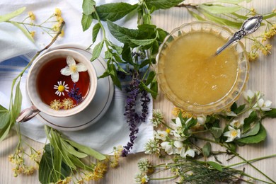 Cup of hot aromatic tea, honey and different fresh herbs on white wooden table, flat lay