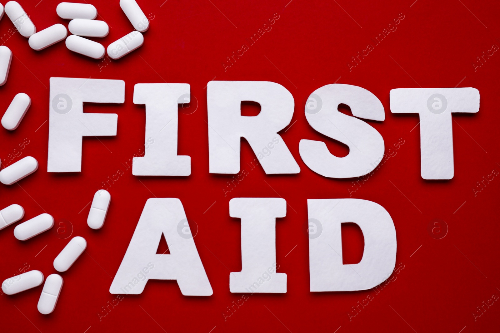 Photo of Words First Aid made of white letters and pills on red background, flat lay