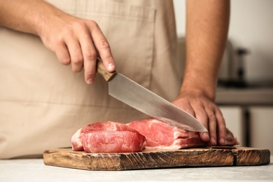 Photo of Man cutting fresh raw meat on table in kitchen, closeup