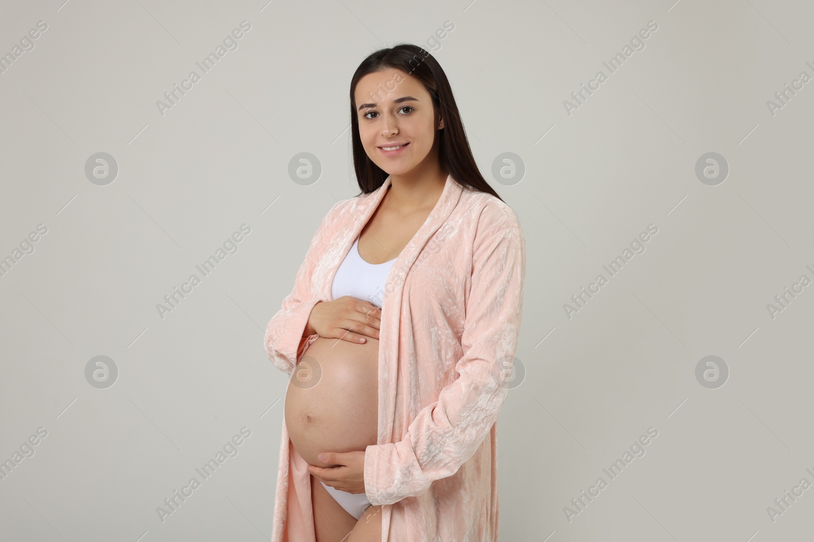 Photo of Beautiful pregnant woman in stylish comfortable underwear and robe on grey background