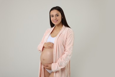 Beautiful pregnant woman in stylish comfortable underwear and robe on grey background