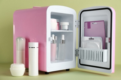 Photo of Open cosmetic refrigerator and skin care products on light green background