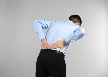 Young man suffering from back pain on light background