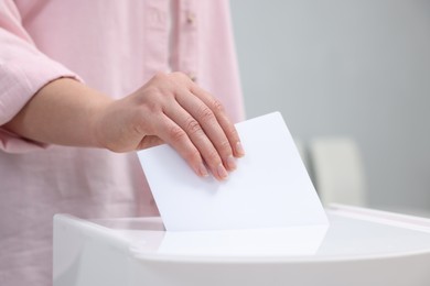 Photo of Woman putting her vote into ballot box on blurred background, closeup